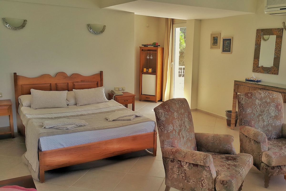 A bedroom with a wooden bed, two chairs, a desk, a mirror, and a window with curtains.