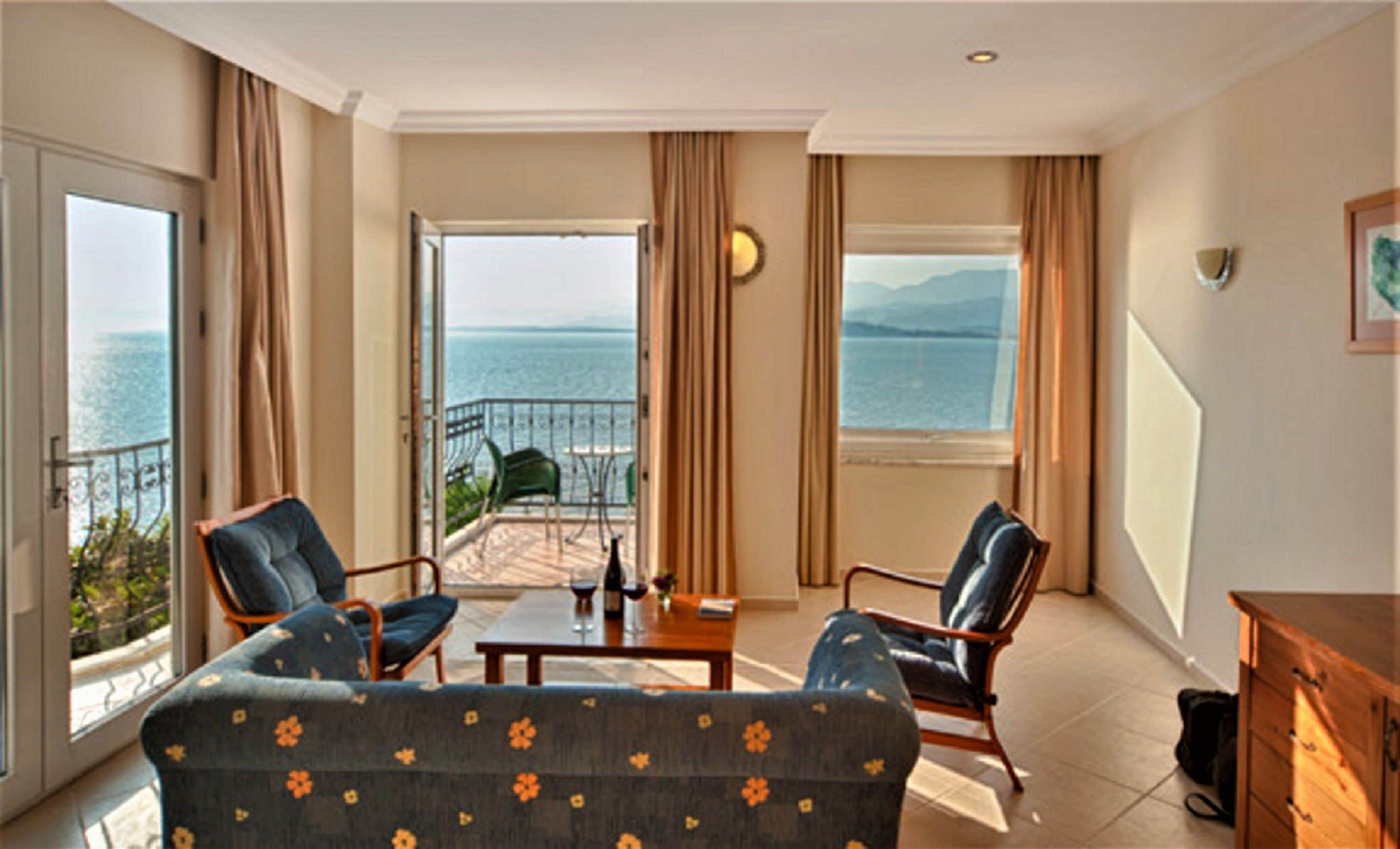 A room with a sofa, two armchairs, a small table, and a view of the sea through large windows.