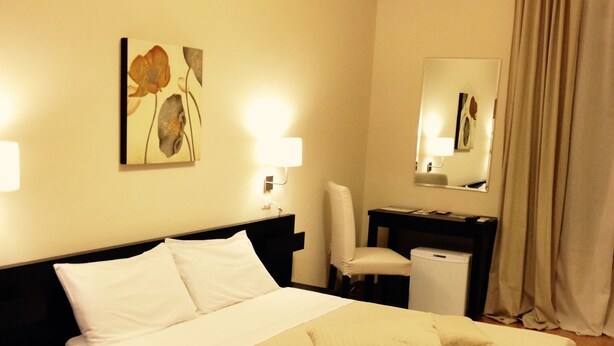 A hotel room with a bed, a desk, a chair, a mirror, and an air conditioning unit. - Bella Cagliari B&B (Cagliari)