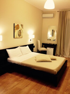 A hotel room with a bed, a desk, a chair, a mirror, and an air conditioning unit. - Bella Cagliari B&B (Cagliari)