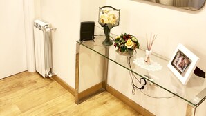 A hotel room with a glass console table, a mirror, framed pictures, a radiator, and a wooden floor. - Bella Cagliari B&B (Cagliari)