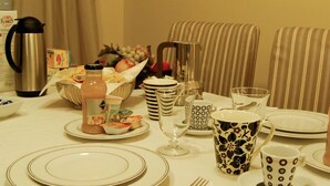 A breakfast table set with plates, cutlery, a fruit bowl, a coffee pot, and various cups and glasses. - Bella Cagliari B&B (Cagliari)