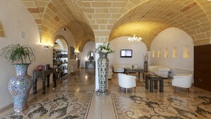 Un vestíbulo amplio con un techo abovedado alto, una columna central con un arreglo floral y una zona de estar con sofás y sillones blancos.