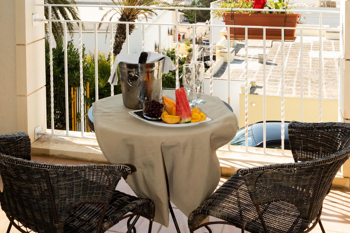 Un balcon avec une table dressée pour deux personnes, un pot de fleurs et une vue sur la mer et le paysage urbain.