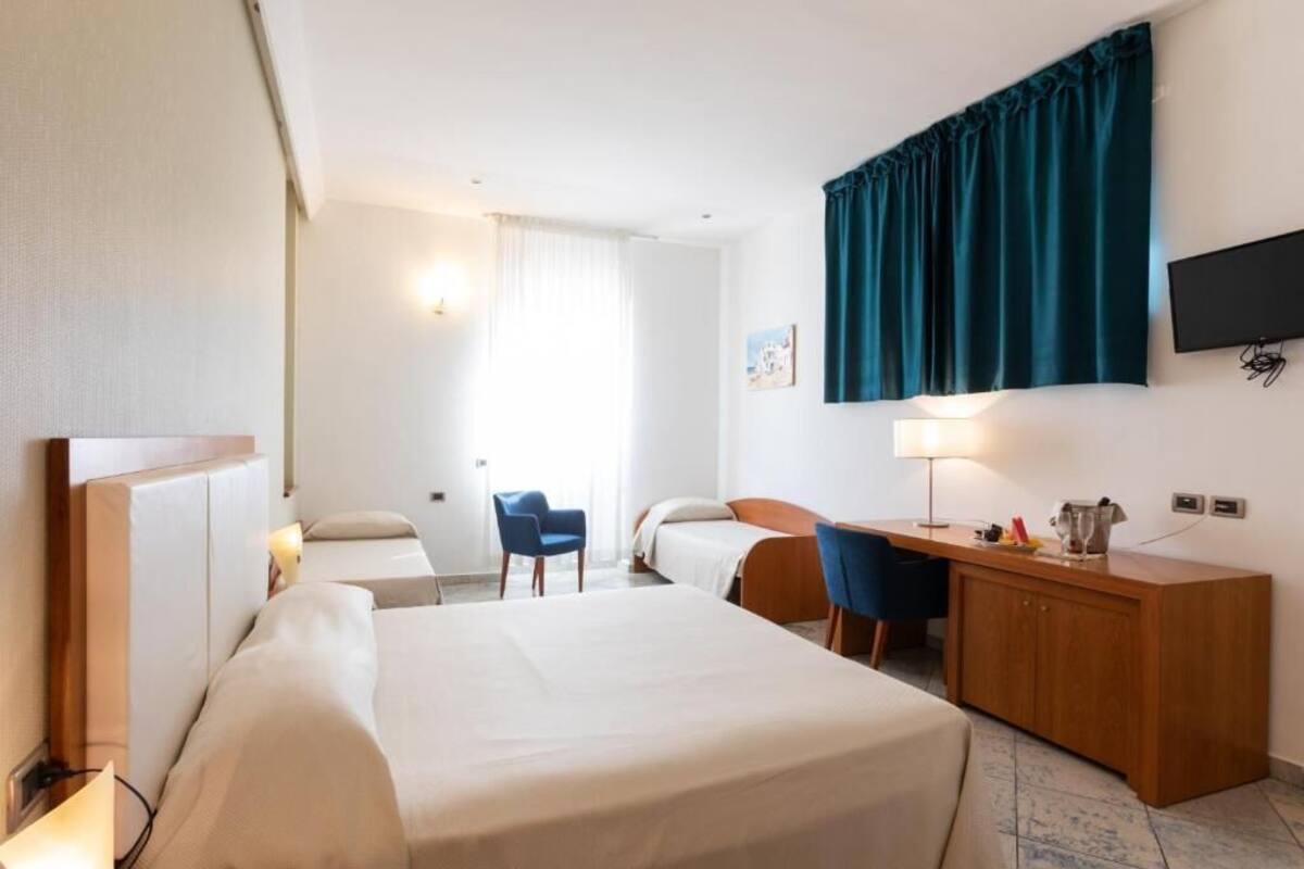 Une chambre d’hôtel équipée d’un lit, d’un bureau, d’une chaise, d’une télévision et d’une fenêtre avec des rideaux.