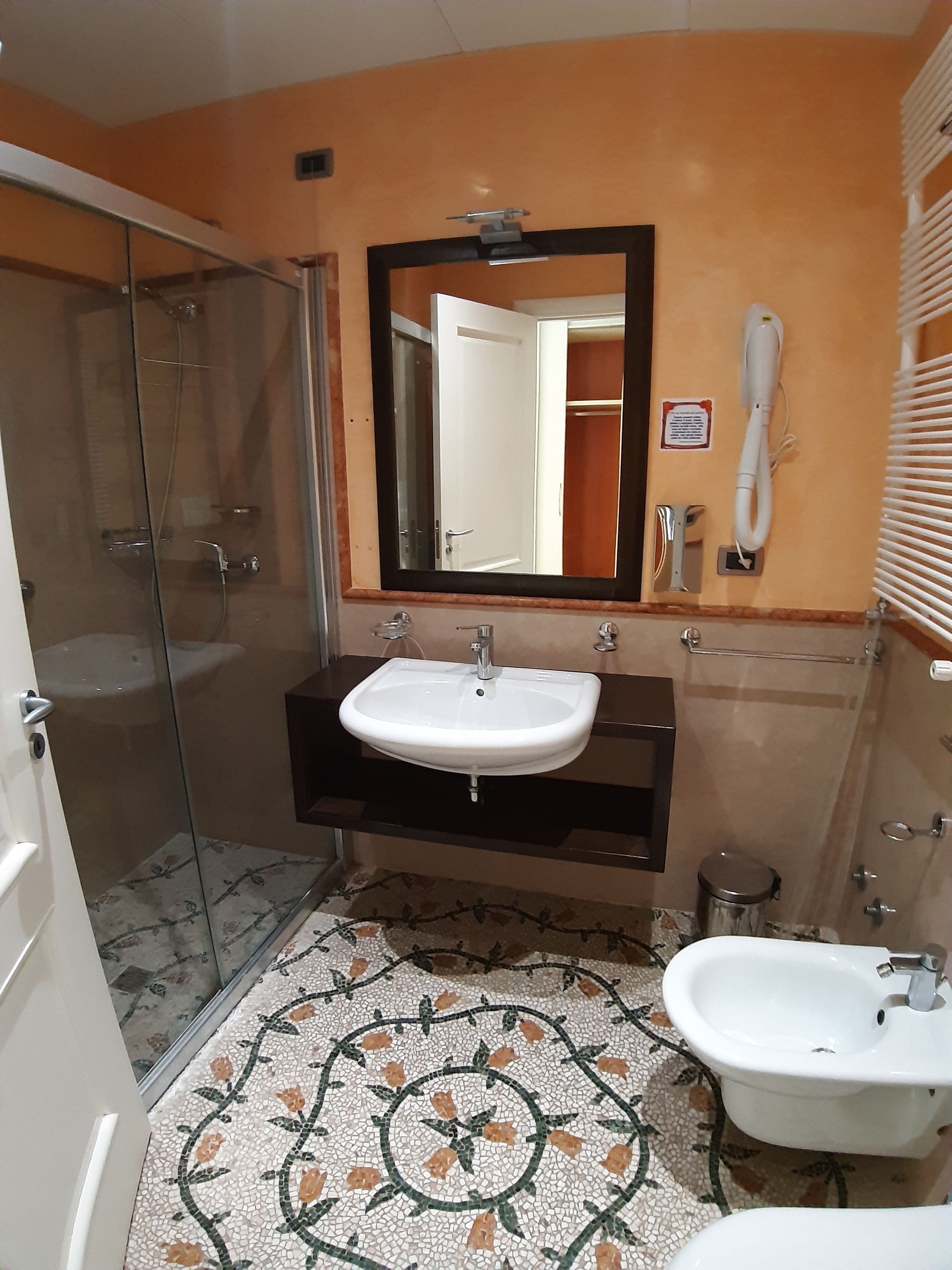 Een badkamer met een douchecabine van glas, een wastafel met spiegel erboven, een toilet en een bidet.