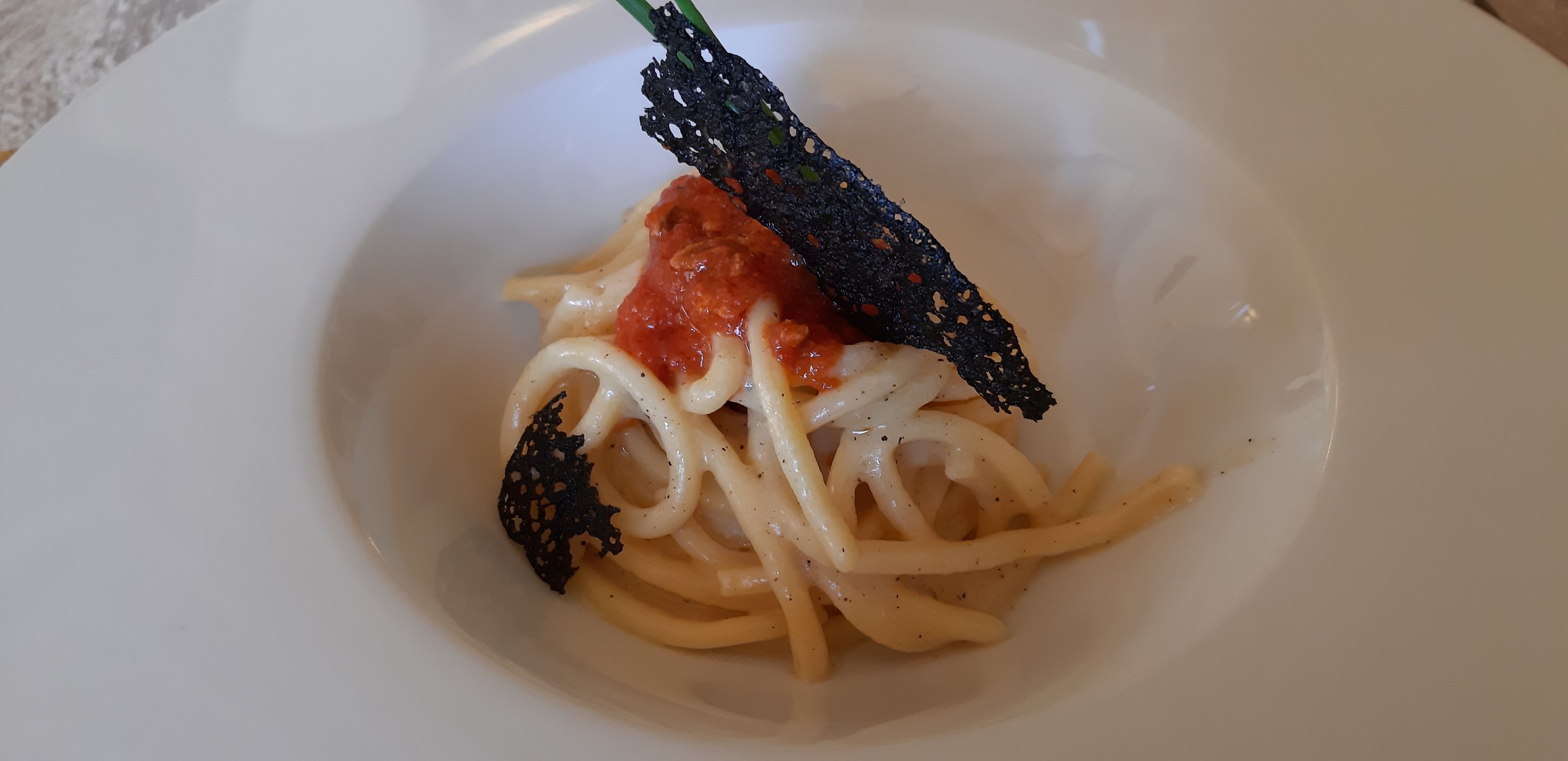 A plate of spaghetti with tomato sauce and black garnish.