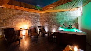 Un área de spa con bancos de madera, una bañera de hidromasaje y paredes de piedra.