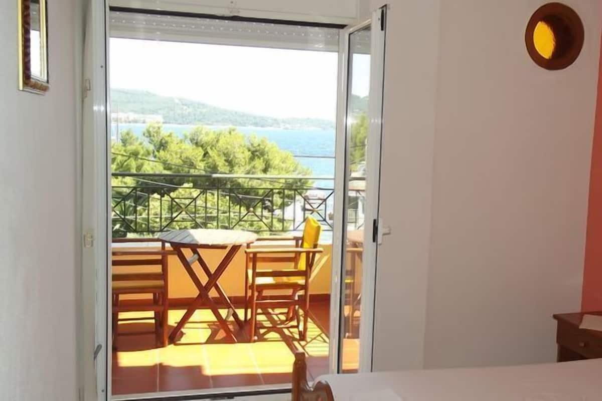 A bedroom with a bed, a nightstand, and a view of a balcony with a table and chairs.