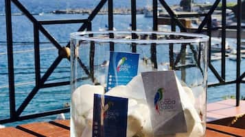 A glass jar filled with white stones on a wooden bench with a metal railing and a view of the sea and boats in the background.