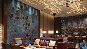 Een moderne lounge met een centrale zithoek, een bar met een wijnrek en een decoratieve plafondlamp.