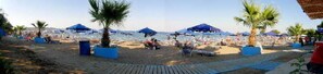 Une plage avec des parasols, des palmiers et des gens.