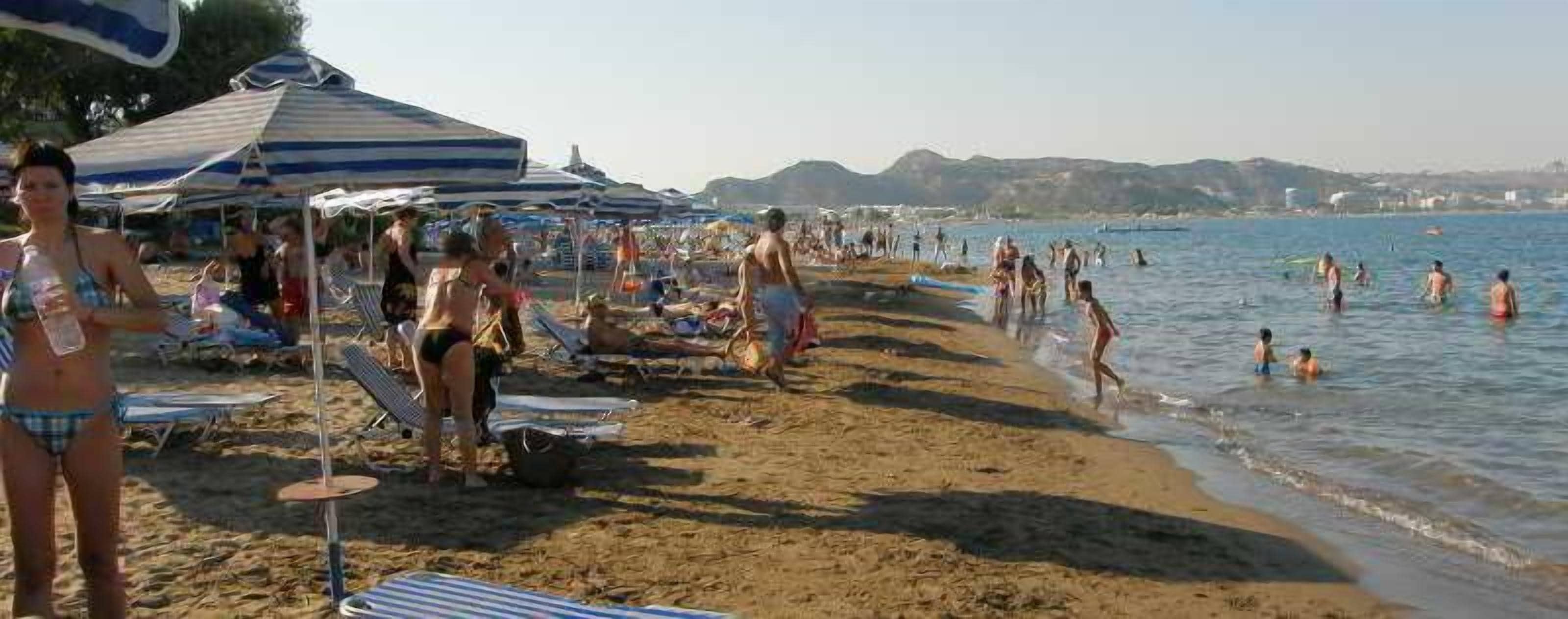 Ein Strand mit Liegestühlen und Sonnenschirmen, Menschen beim Schwimmen und Spazierengehen am Ufer.