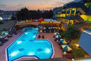 A swimming pool with lounge chairs and umbrellas, surrounded by buildings with balconies. - Grecian Fantasia Resort (Rhodes)