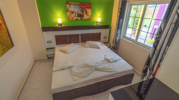 Une chambre d’hôtel avec un lit, des oreillers, un mur d’accent vert et une fenêtre avec des rideaux.