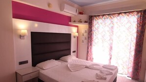 Une chambre à coucher avec un grand lit, des tables de chevet, un climatiseur fixé au mur et une fenêtre ornée de rideaux à motifs.