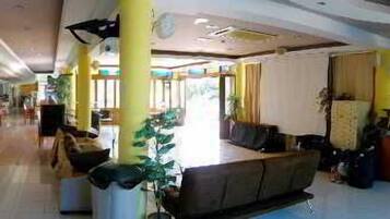 A spacious hotel lobby with a central seating area, multiple dining tables, and a large window providing natural light.