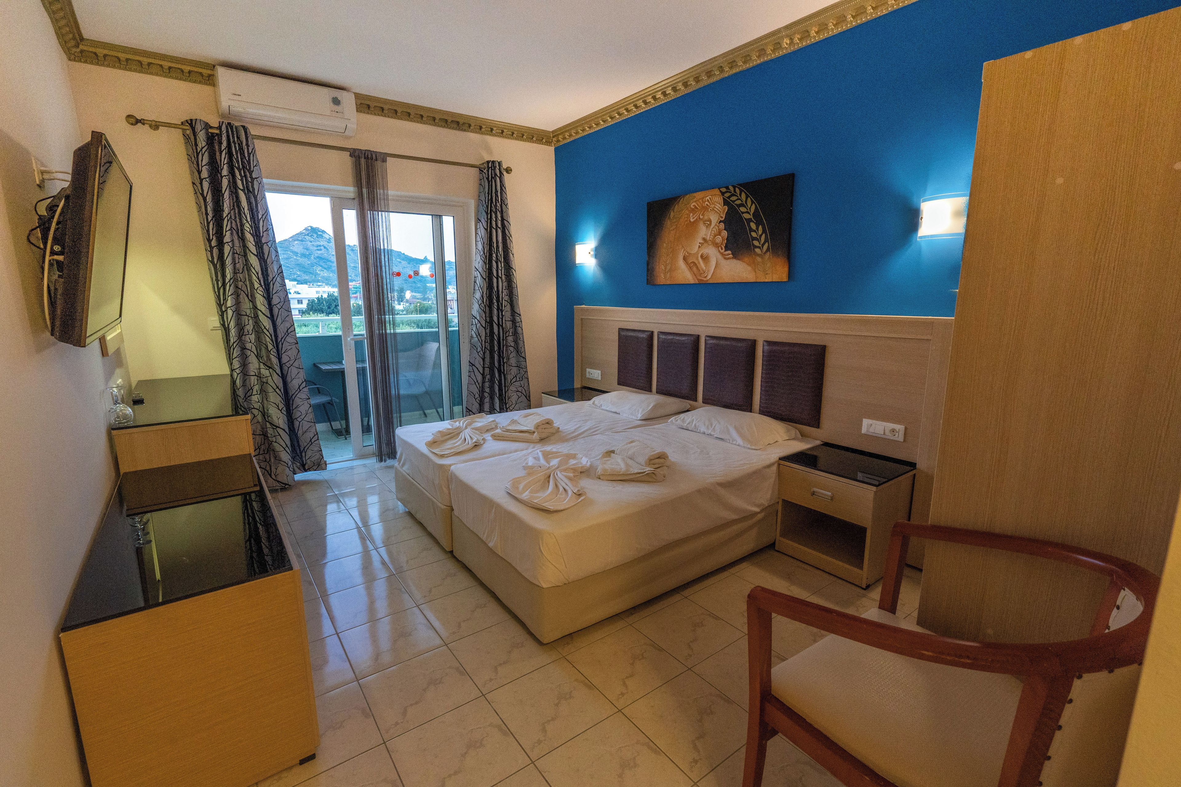 Habitación de hotel con una cama, un escritorio, una silla, un televisor y vistas al exterior.