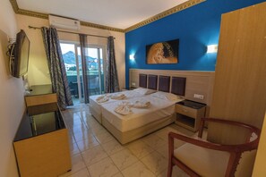 A hotel room with a bed, a desk, a chair, a TV, and a view of the outside. - Grecian Fantasia Resort (Rhodes)