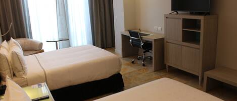 A hotel room with two beds, a desk, a chair, a television, and a lamp.