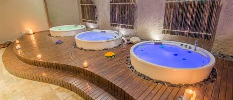 A spa area with three hot tubs arranged in a semi-circular layout, surrounded by wooden decking and stone tiles.