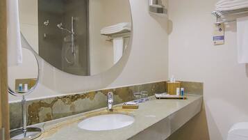 A bathroom with a round mirror, a sink, a towel rack, and a glass shower enclosure.