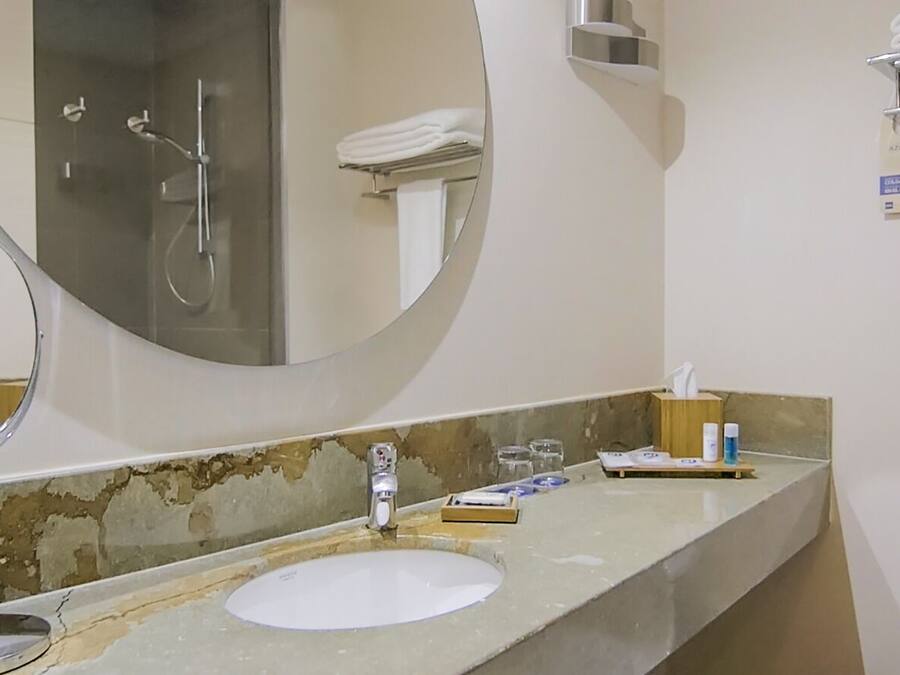 A bathroom with a round mirror, a sink, a towel rack, and a glass shower enclosure.