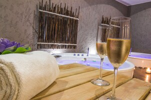 Zona de spa con un banco de madera, dos copas de champán, una bañera y una pared decorativa.