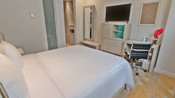 A hotel room with a large bed, a desk with a chair, a TV, a mirror, and a small bathroom area.