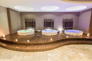 Un área de spa con tres tinas de hidromasaje, escalones de madera y velas.