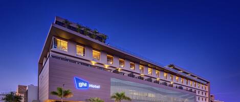A modern hotel with a flat roof, multiple balconies, and a large glass facade.