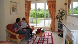 A living room with a sofa, a coffee table, a television, and a window with curtains. - Gort na Coiribe Holiday Village (Galway)