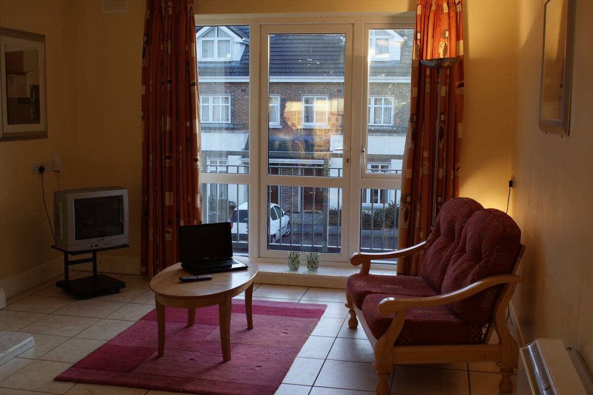 Een woonkamer met een bank, een kleine tafel, een televisie en een raam met gordijnen.