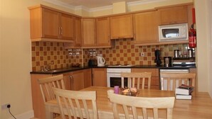 A compact kitchen with wooden cabinets, a microwave, a coffee maker, and a dining table with chairs. - Gort na Coiribe Holiday Village (Galway)