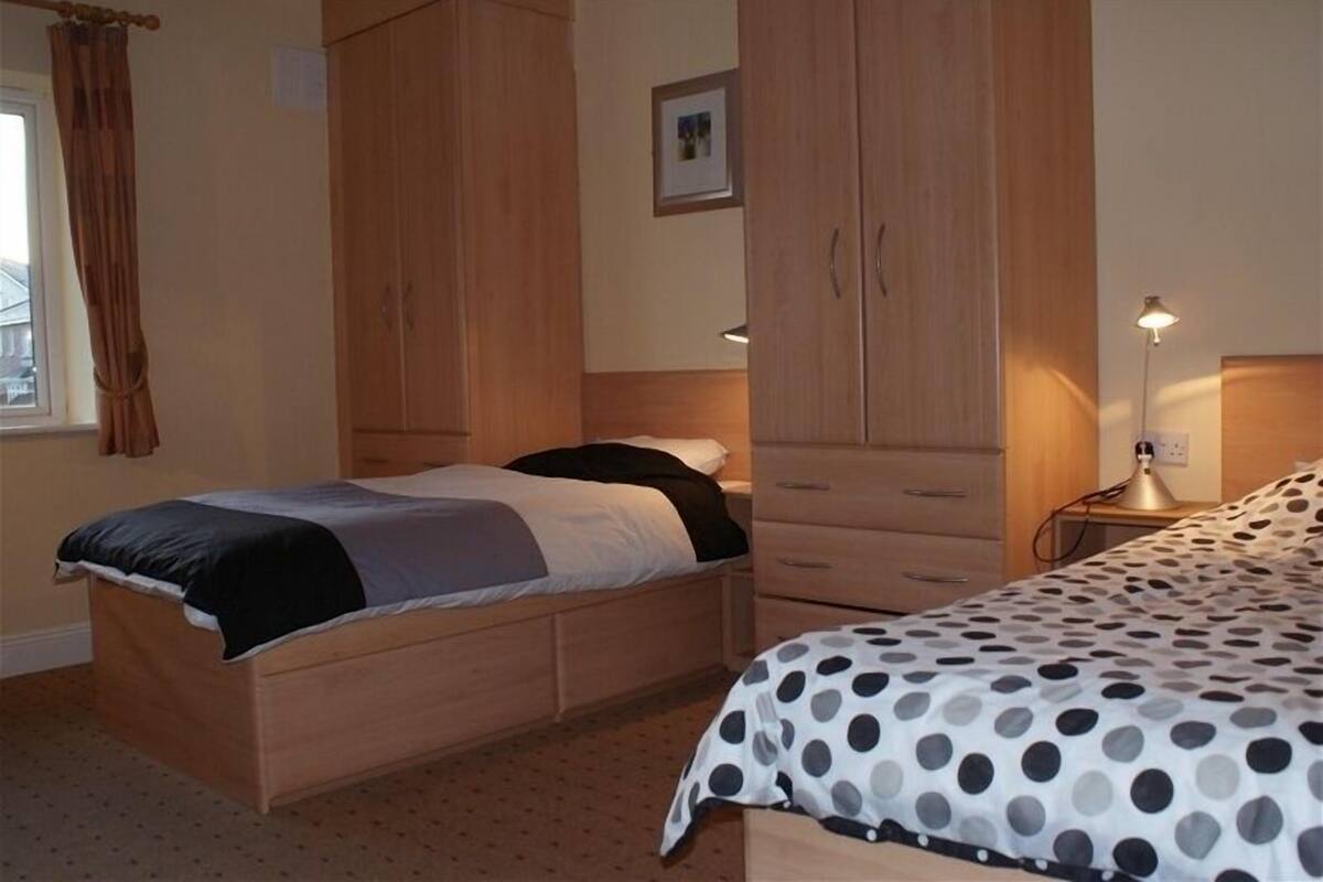 Een slaapkamer met een houten bed, een nachtkastje, een lamp en een kledingkast.