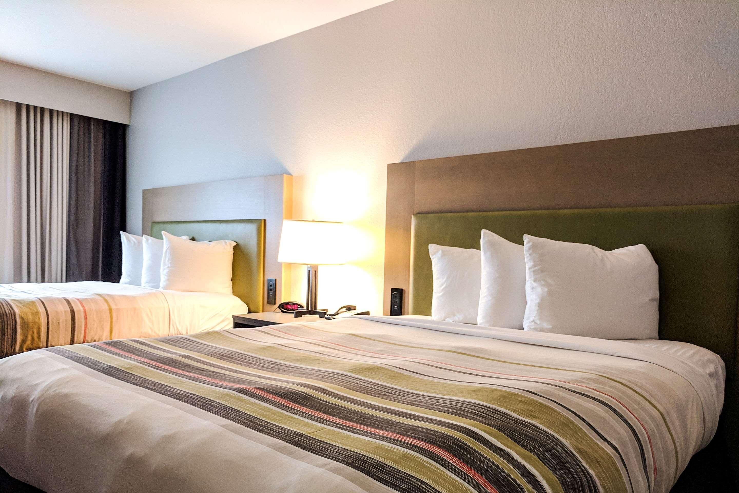 Une chambre d’hôtel avec deux lits, une couvre-lit à rayures, une tête de lit verte et une lampe sur la table de chevet.