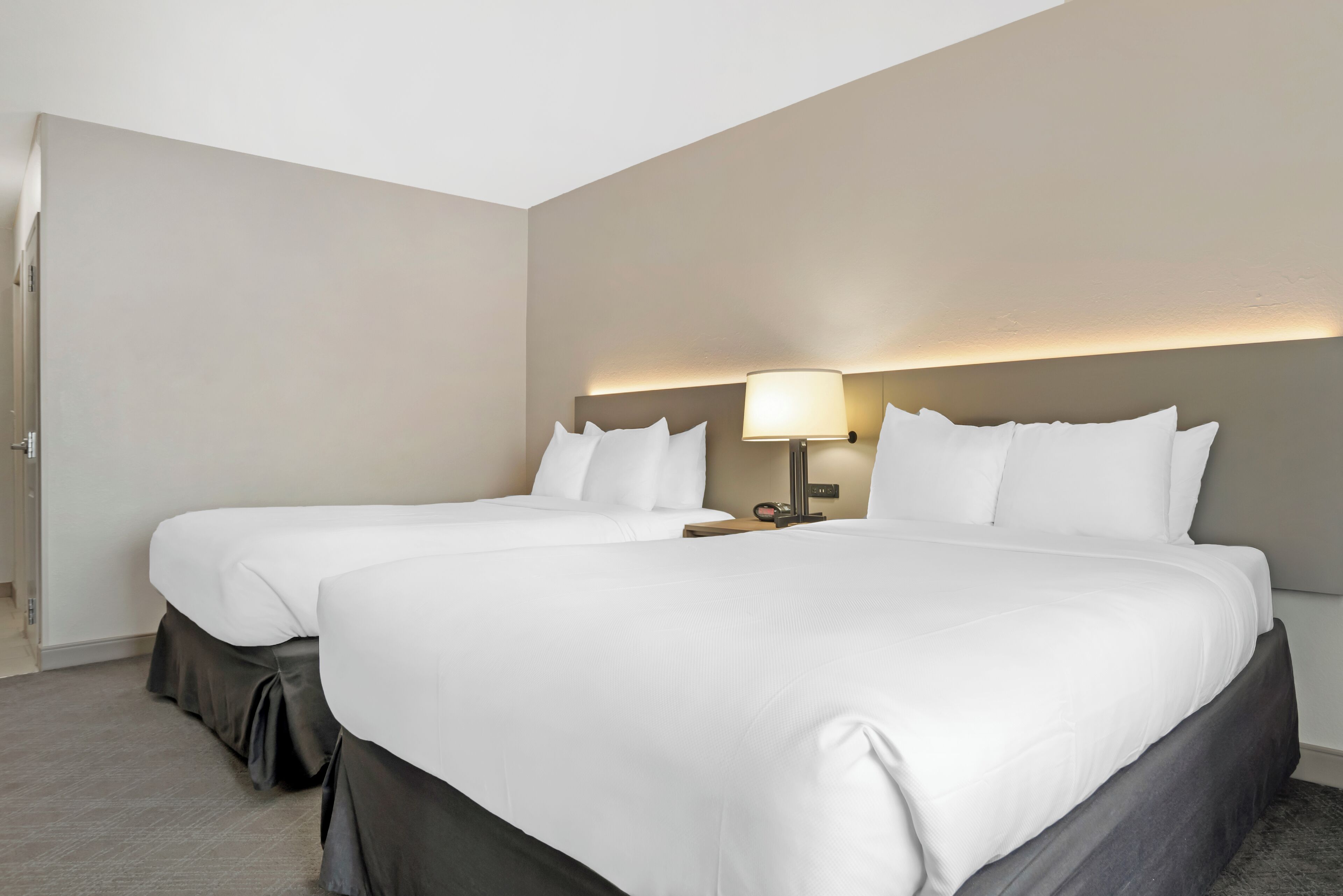 A hotel room with two beds, a nightstand with a lamp, and a door.