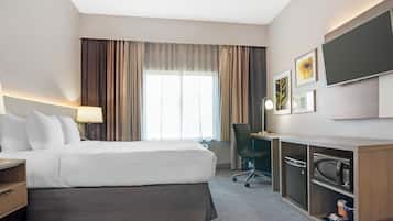 A hotel room with a bed, desk, chair, and a flat-screen TV.