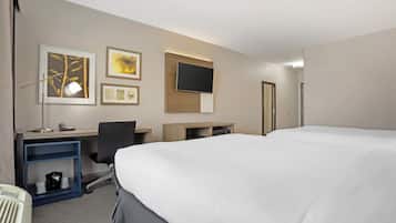 Ett hotellrum med en stor säng, ett skrivbord med en stol, en tv som är monterad på väggen och en hylla med en lampa och en telefon.