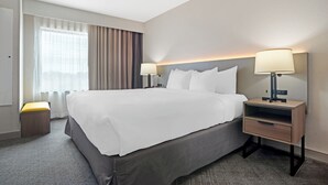 A hotel room with a large bed, two bedside tables with lamps, a small stool, and a window with curtains. - Comfort Inn & Suites Slidell - New Orleans Area (Slidell)