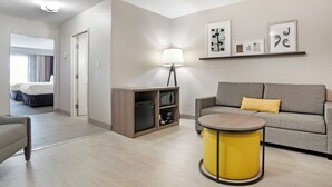 A modern hotel room with a sofa, a small table, a lamp, and artwork on the wall. - Comfort Inn & Suites Slidell - New Orleans Area (Slidell)