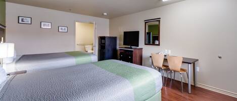 A hotel room with two beds, a desk, a chair, a television, and a mirror.