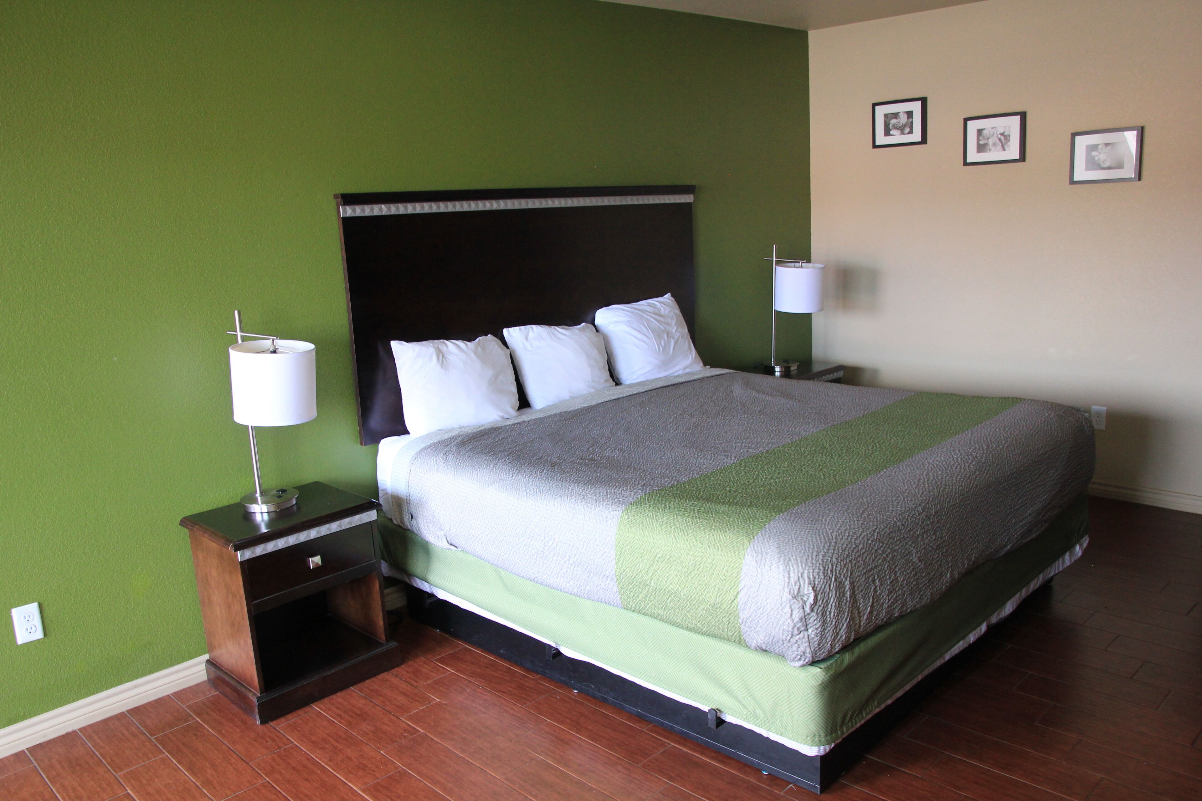 A neatly made bed with a green and white bedspread, a wooden nightstand with a lamp, and a wall with three framed pictures.