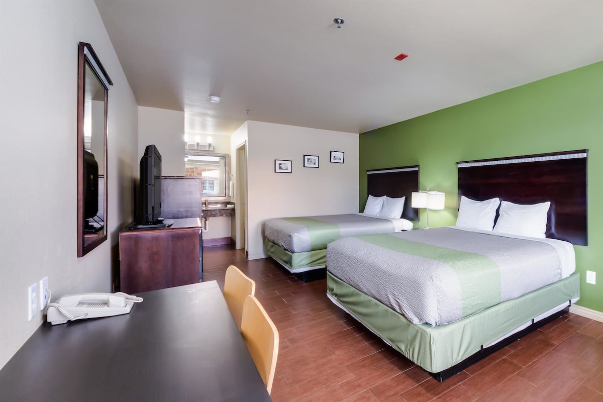 A hotel room with two beds, a desk, a chair, a TV, and a bathroom visible in the background.