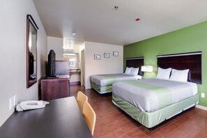 A hotel room with two beds, a desk, a chair, a TV, and a bathroom visible in the background.