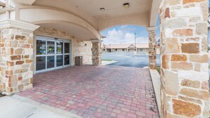 A covered entrance with stone pillars, a brick-paved area, and a glass door leading to a building. - Eagle Ford Inn (Floresville)