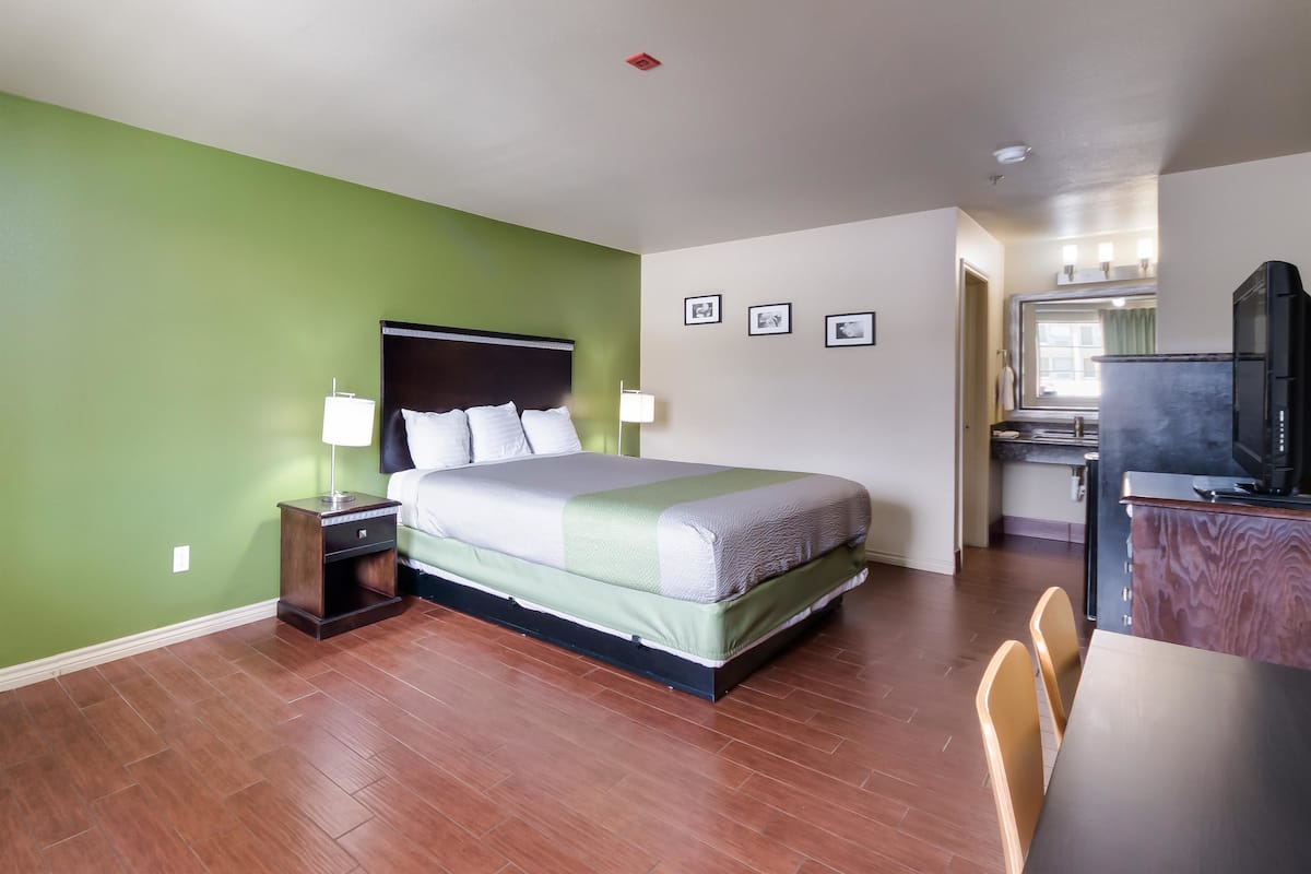 A hotel room with a bed, bedside tables, a desk, and a kitchenette.