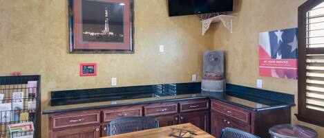 A restaurant with a wooden table, chairs, a TV mounted on the wall, and a framed picture above the counter.
