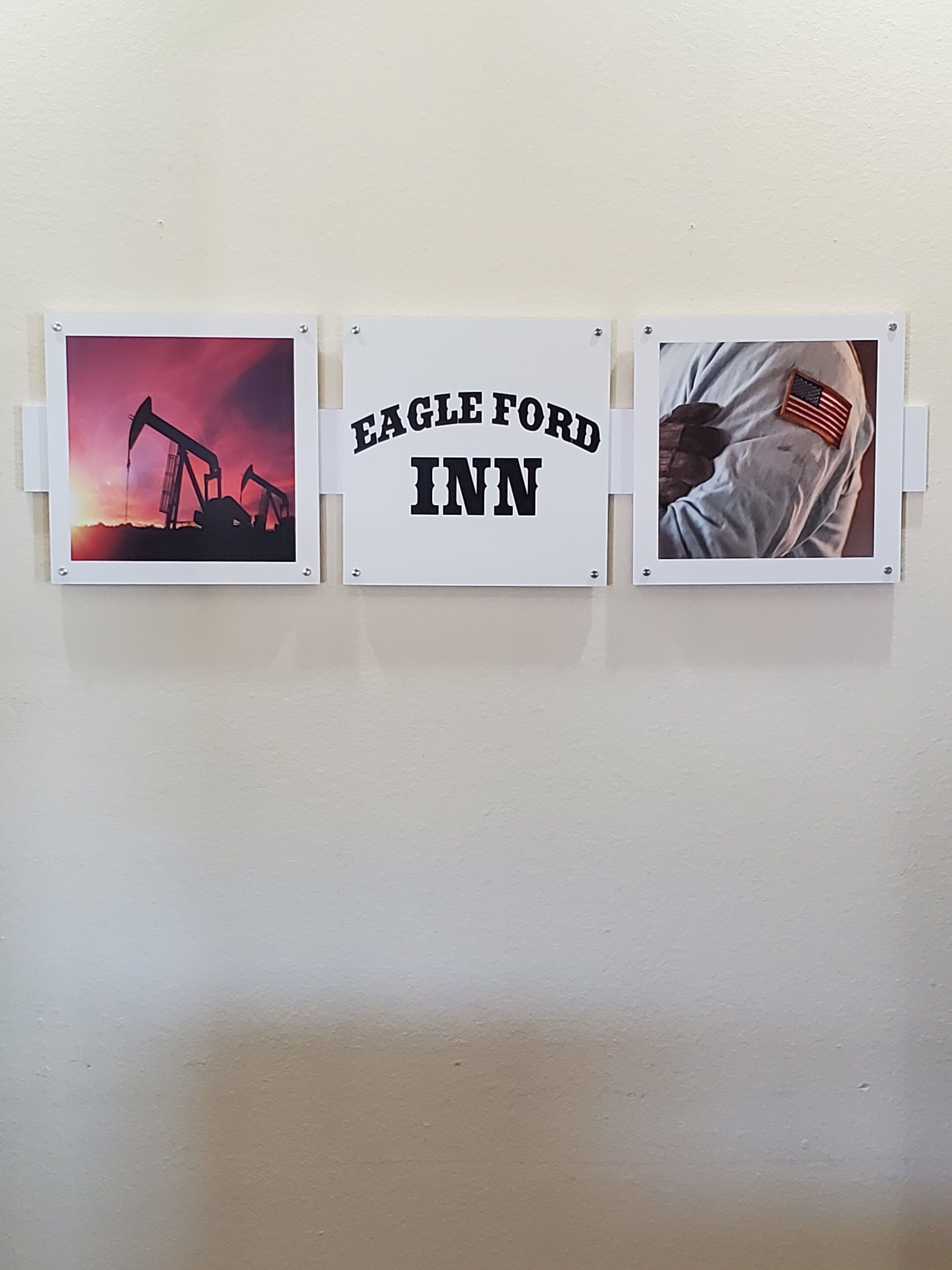 Three framed pictures on a wall: an oil rig at sunset, a sign reading "Eagle Ford Inn," and a person in military uniform with an American flag patch.