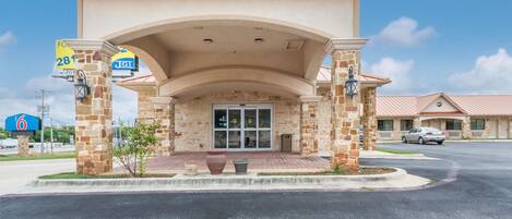 A hotel entrance with a stone facade, a covered patio, and a clear sky.